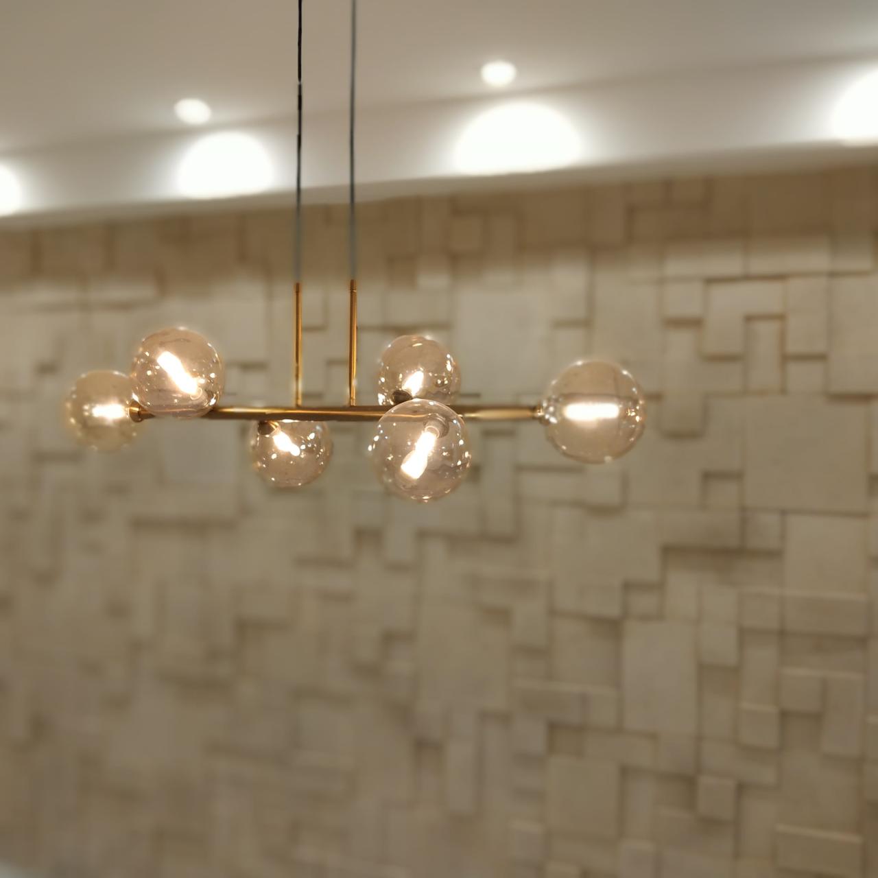 Detalhe de luminária contemporânea com pendentes de vidro em parede com revestimento geométrico 3D, evidenciando acabamento premium.