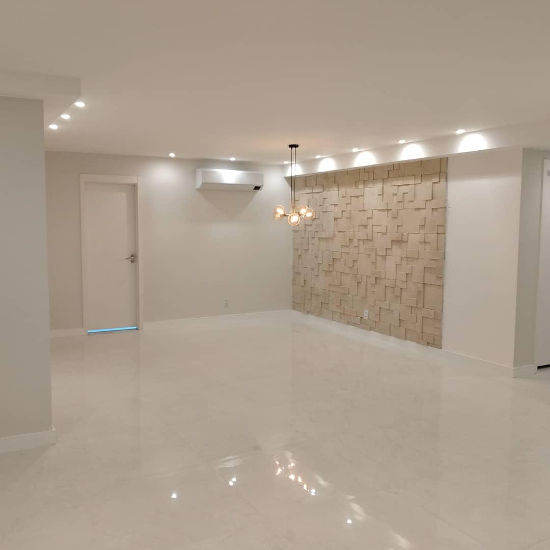 Ambiente residencial de alto padrão finalizado com parede de painel 3D geométrico, piso porcelanato polido, iluminação embutida e pendente decorativo.