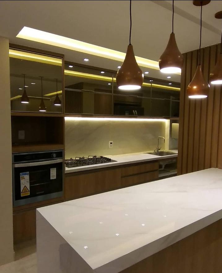 Cozinha de alto padrão com ilha em painel amadeirado, pendentes em cobre, marcenaria sob medida e iluminação embutida.