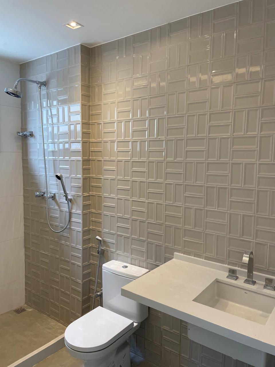 Banheiro com revestimento 3D bege, metais cromados e bancada em mármore, demonstrando acabamento premium em obra residencial.
