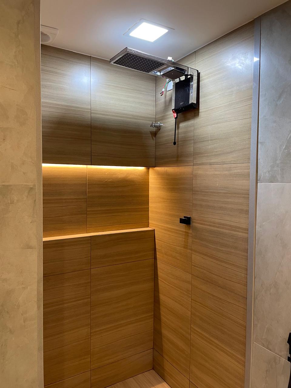 Box de banho com acabamento premium em porcelanato amadeirado, chuveiro de teto e iluminação em LED embutida.
