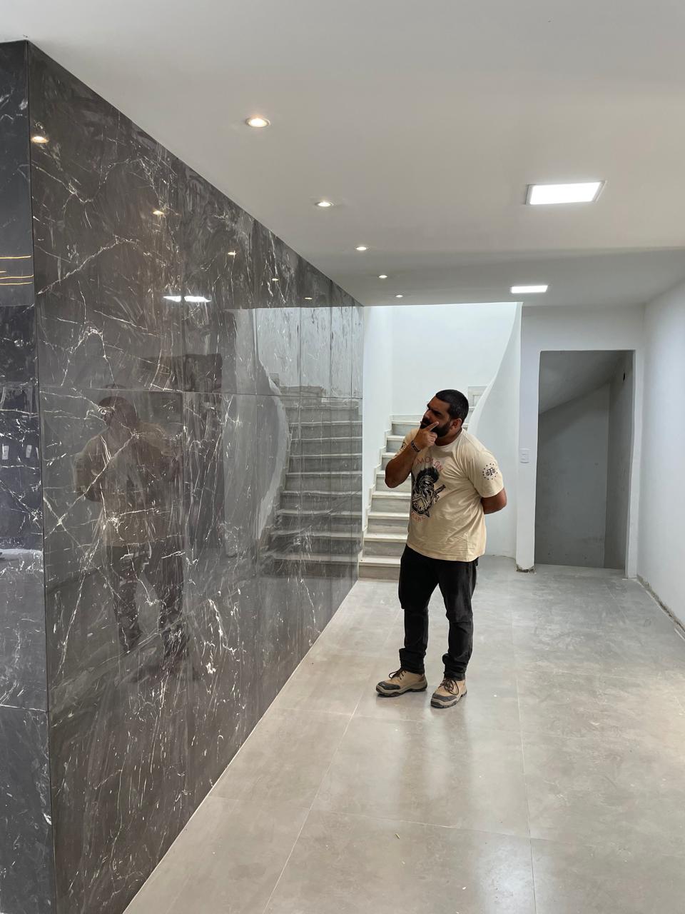 Ambiente residencial de alto padrão entregue com parede revestida em mármore preto, escada em mármore e piso polido, exibindo o acabamento premium da obra.