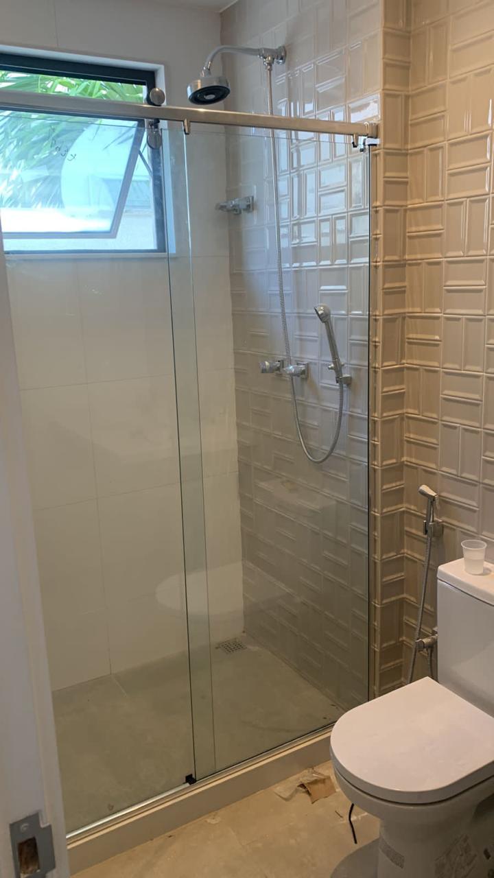 Banheiro de alto padrão com box de vidro, chuveiro tipo chuva, revestimento em relevo e ducha higiênica, exemplo de acabamento premium executado pela Eretz.