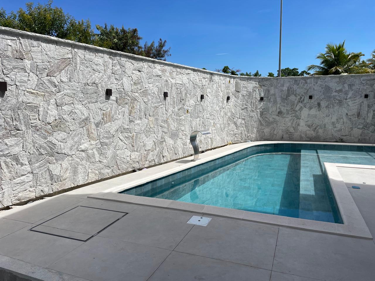 Área de lazer com piscina revestida em pedra natural irregular, iluminação embutida e detalhe em aço inox, acabamento premium de alto padrão.