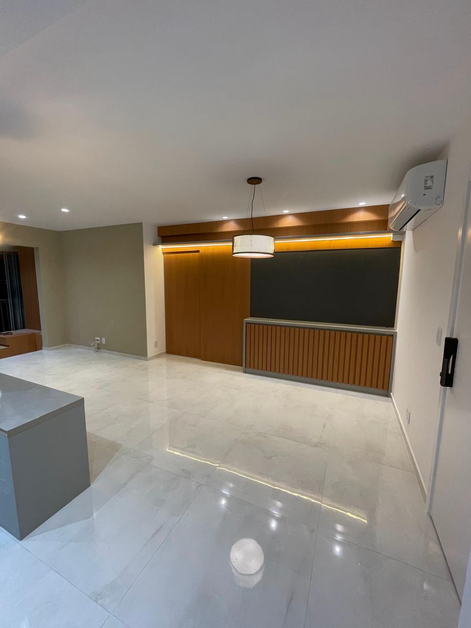 Interior residencial de alto padrão entregue com piso porcelanato polido, painel ripado em madeira, iluminação embutida e pendente moderno.