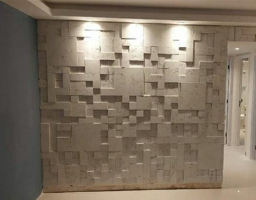 Painel de acabamento 3D em pedra natural com iluminação embutida, demonstrando trabalho premium de revestimento em ambiente residencial.