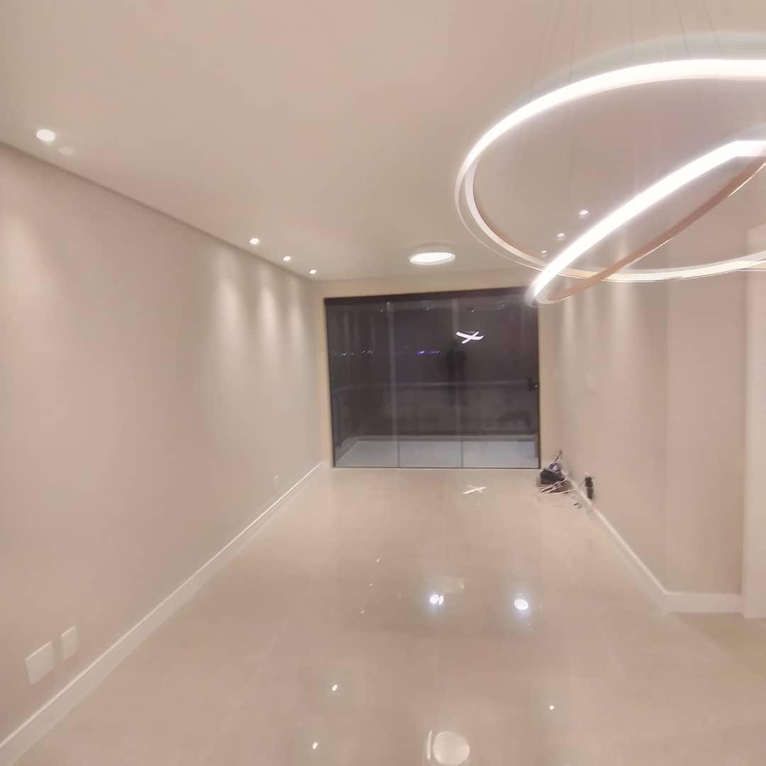 Ambiente residencial de alto padrão finalizado com piso polido espelhado, paredes em acabamento laca branca, iluminação embutida e pendente LED circular.