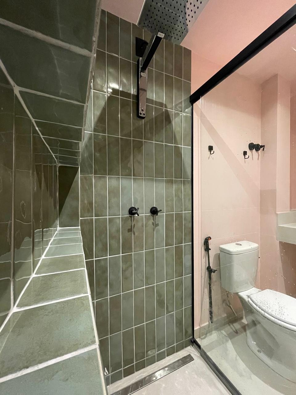 Banheiro com box em revestimento verde, metais pretos e box de vidro.